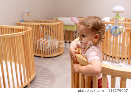Toddler standing and playing in crib in modern nursery filled with some wooden cribs 118179097