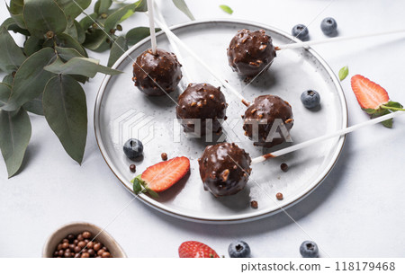 Chocolate cake pops with nuts on a plate with fresh berries on a light background.  118179468