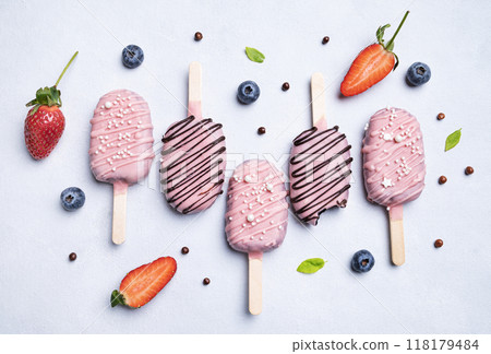 Flat lay of  cake pops ice cream on a stick in pink glaze with strawberries and blueberries  118179484