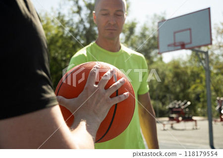 Two basketball players holding orange ball on sports court. Sports goals competition game, champion outdoor workout. Close up. Game moment. Two basketball players holding orange ball on sports court. Sports goals competition game, champion outdoor workout. Close up. Game moment. 118179554