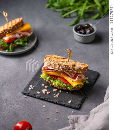 Club sandwich on a board with a bacon, cheese, tomato and lettuce on a dark background Club sandwich on a board with a bacon, cheese, tomato and lettuce on a dark background 118179774