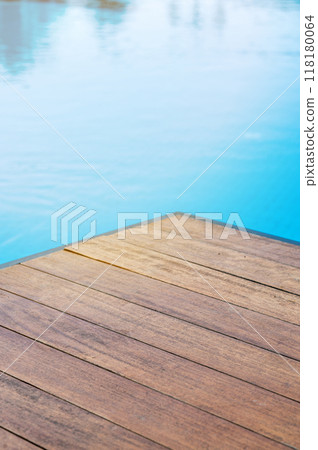 Empty wooden tabletop in front of a swimming pool with blue tiles. 118180064
