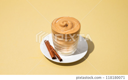 Dalgona coffee. Whipped instant iced coffee in a glass with cinnamon sticks on yellow background. 118180071