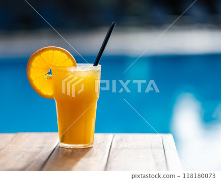 Freshly squeezed orange juice on a wooden tabletop in front of the pool.  118180073