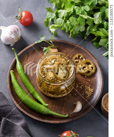 Jalapeno hot pepper, sliced in a jar with spices on a wooden plate with fresh vegetables 118180075