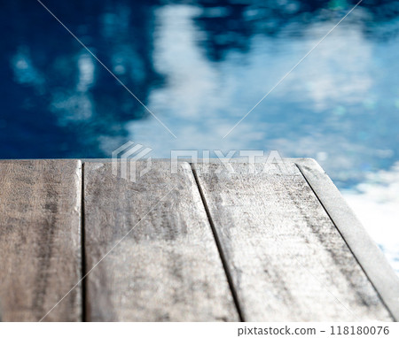 Empty wooden tabletop in front of a swimming pool with blue water close up and blur.  118180076