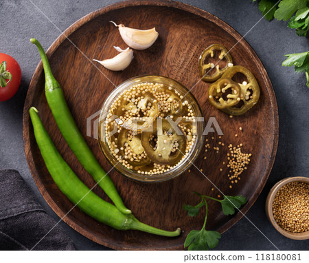 Jalapeno hot pepper, sliced in a jar with spices on a wooden plate with fresh vegetables  118180081