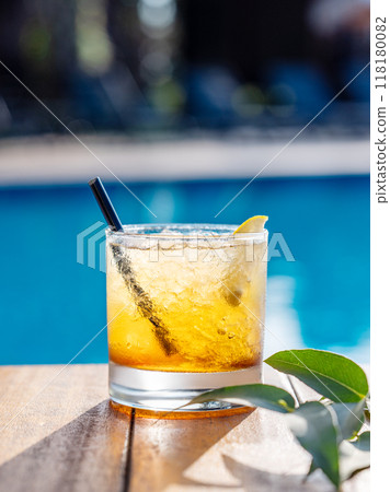 Alcohol cocktail with lemon on a wooden tabletop in front of the pool close-up. 118180082