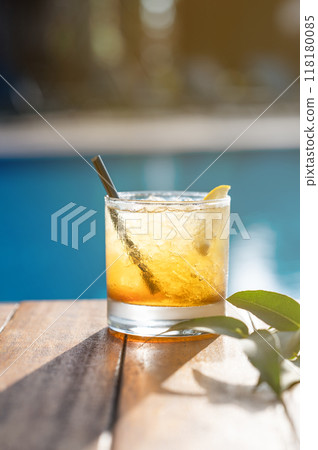Alcohol cocktail with lemon on a wooden tabletop in front of the pool close-up. Alcohol cocktail with lemon on a wooden tabletop in front of the pool close-up. 118180085