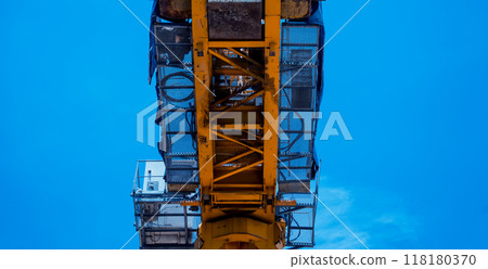 A large yellow crane stands out against a bright blue sky 118180370