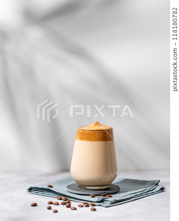 Dalgona coffee. Whipped instant coffee in a glass with beans and shadow on a light background. Dalgona coffee. Whipped instant coffee in a glass with beans and shadow on a light background. 118180782