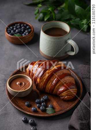 Freshly baked chocolate croissant with blueberries on a wooden plate on a dark background  118180793