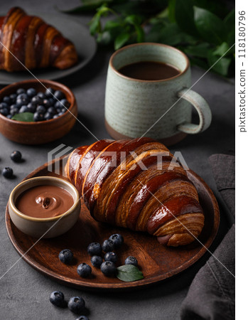 Freshly baked chocolate croissants with blueberries on a wooden plate on a dark background Freshly baked chocolate croissants with blueberries on a wooden plate on a dark background 118180796