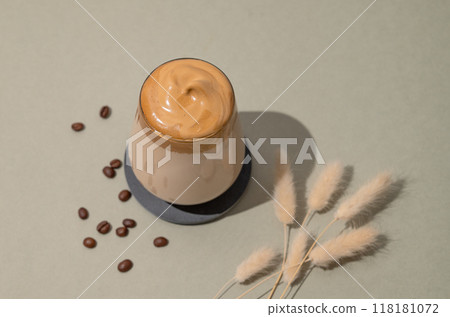 Dalgona coffee. Whipped instant coffee in a glass with beans and dry flowers on green background. Dalgona coffee. Whipped instant coffee in a glass with beans and dry flowers on green background. 118181072