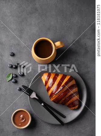 Freshly baked chocolate croissant with blueberries on a gray plate on a dark background  118181075