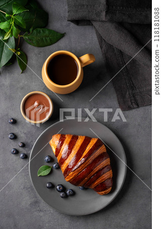 Freshly baked chocolate croissant with blueberries on a gray plate on a dark background 118181088