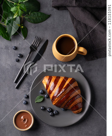 Freshly baked chocolate croissant with blueberries on a gray plate on a dark background  118181091