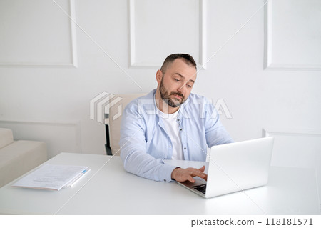 A man with a beard looks at the laptop screen with surprise and disbelief. A man with a beard looks at the laptop screen with surprise and disbelief. 118181571