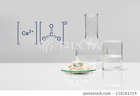 Calcium carbonate chip in chemical watch glass with molecular structure place next to beaker and Flat Bottom Flask on white laboratory table. Side view Calcium carbonate chip in chemical watch glass with molecular structure place next to beaker and Flat Bottom Flask on white laboratory table. Side view 118181724