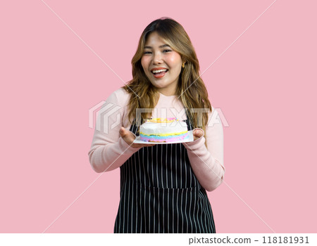 Young asian woman with an apron in celebratory or festive mood holding colorful cake with various sprinkles on the topping. Portrait on pink background with studio light. Isolated 118181931