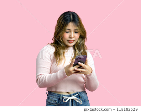 Young asian woman in casual clothing, holding and looking at a smartphone. Portrait on a simple pink background with studio light. Isolated Young asian woman in casual clothing, holding and looking at a smartphone. Portrait on a simple pink background with studio light. Isolated 118182529