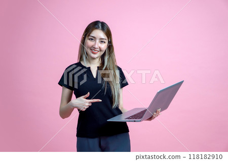 Young asian woman stand with a smile, pointing at laptop computer monitor. Portrait on pink background with studio light. Young asian woman stand with a smile, pointing at laptop computer monitor. Portrait on pink background with studio light. 118182910