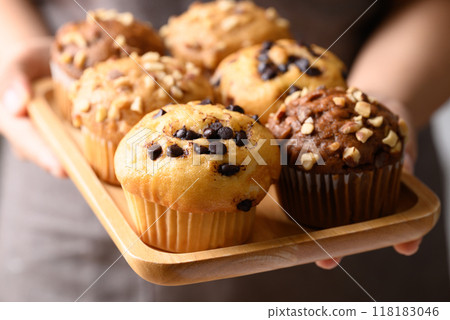 Vanilla chocolate chips muffin, Chocolate almond muffin and Vanilla almond muffin on wooden plate holding by hand Vanilla chocolate chips muffin, Chocolate almond muffin and Vanilla almond muffin on wooden plate holding by hand 118183046