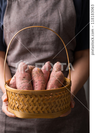 Raw organic Japanese sweet potatoes in basket holding by hand 118183063