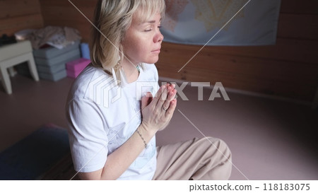 A woman practices meditation at home, sitting on a mat on the floor. Mindfulness meditation concept. Well-being. 118183075