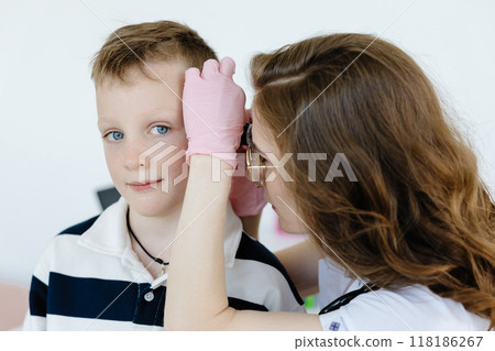 Female doctor examining boy's ear with otoscope in office. Ear cavity treatment health checkup 118186267