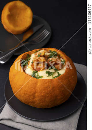Whole baked pumpkin with tiger prawns, melted cheese and tomatoes. Traditional dish of Brazil, home cooking. Selective focus, close-up, black background. 118186437