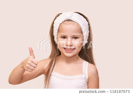 Smiling girl with headband giving thumbs up in delightful expression on light 118187073
