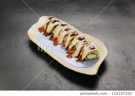 Eel sushi roll with creamy filling, topped with savory sauce and sesame seeds on a stylish plate 118187202