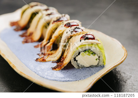 Eel sushi roll with creamy filling, topped with savory sauce and sesame seeds on a stylish plate 118187205