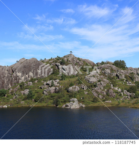 Small blue lake and single tree growing on top of a rocky hill, Hellvik, Norway. Small blue lake and single tree growing on top of a rocky hill, Hellvik, Norway. 118187745