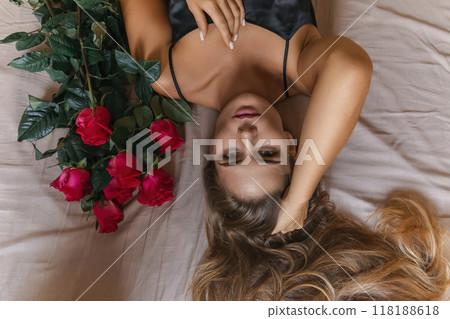 A woman is laying on a bed with a bouquet of red roses next to her. Concept of romance and intimacy, as the woman is surrounded by the flowers and he is in a relaxed and comfortable position. A woman is laying on a bed with a bouquet of red roses next to her. Concept of romance and intimacy, as the woman is surrounded by the flowers and he is in a relaxed and comfortable position. 118188618
