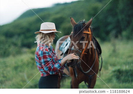 Happy blonde with horse in forest. Woman and a horse walking through the field during the day. Dressed in a plaid shirt and black leggings. Happy blonde with horse in forest. Woman and a horse walking through the field during the day. Dressed in a plaid shirt and black leggings. 118188624
