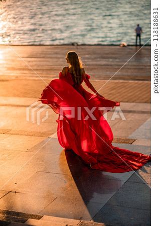 Sunrise red dress. A woman in a long red dress against the backdrop of sunrise, bright golden light of the sun's rays. The concept of femininity, harmony. 118188631