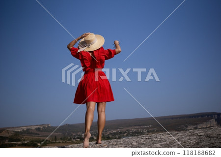 A woman in a red dress is standing on a rocky hillside, wearing a straw hat A woman in a red dress is standing on a rocky hillside, wearing a straw hat 118188682