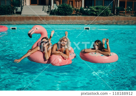 Three women are floating in the pool on inflatable floats. One of the floats is pink and has a flamingo on it. The women are smiling and enjoying their time in the water. 118188912