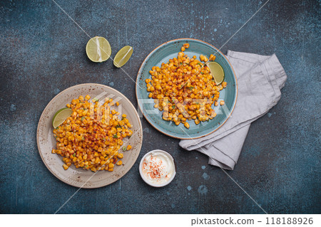 Two plates of esquites mexican street corn salad with chili, mayonnaise, and lime on dark stone background 118188926