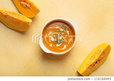 Bowl of creamy pumpkin soup decorated with parsley and pepper on warm yellow beige background top view Bowl of creamy pumpkin soup decorated with parsley and pepper on warm yellow beige background top view 118188945