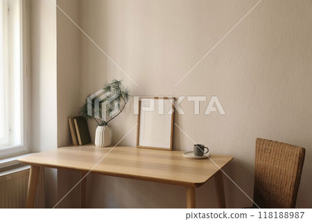 Cozy Christmas interior. Minimal winter home composition. Blank vertical wooden picture frame mockup, cup of coffee on table near window. Pine tree branches, white vase. Beige wall background 118188987