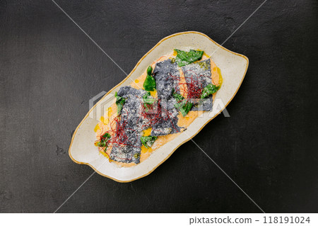 Gourmet squid ink ravioli with vibrant garnishes in a creamy sauce - an elegant and artistic dish 118191024