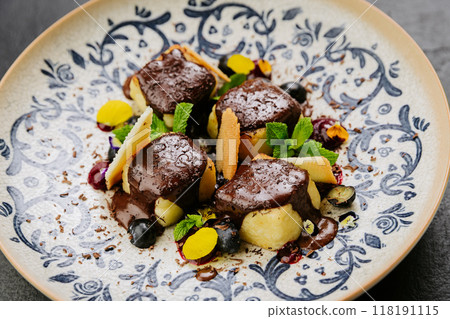 Chocolate-covered gourmet dessert with fresh mint, biscuit shards, and berries on a decorative plate 118191115