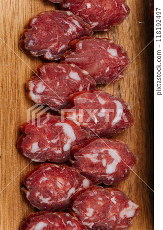 Close-up of thinly sliced salami on a wooden board, showcasing rich marbling and gourmet quality 118192497