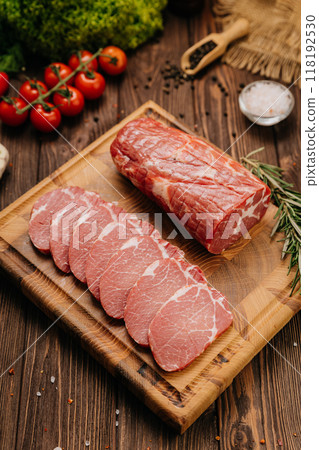 Raw pork loin with rosemary and fresh tomatoes on cutting board, perfect for culinary presentations Raw pork loin with rosemary and fresh tomatoes on cutting board, perfect for culinary presentations 118192530