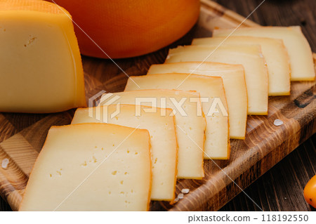 Wheel and slice of cheese on cutting board, perfect for culinary displays and gourmet presentations Wheel and slice of cheese on cutting board, perfect for culinary displays and gourmet presentations 118192550