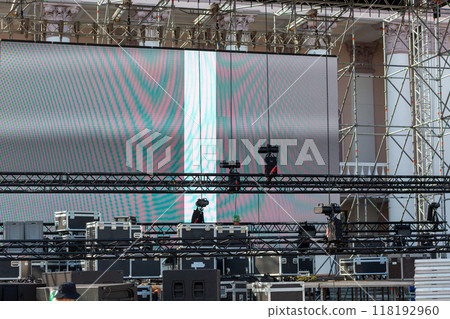 Stacks of sound equipment and lighting gear are arranged at an outdoor venue, ready for a concert. 118192960