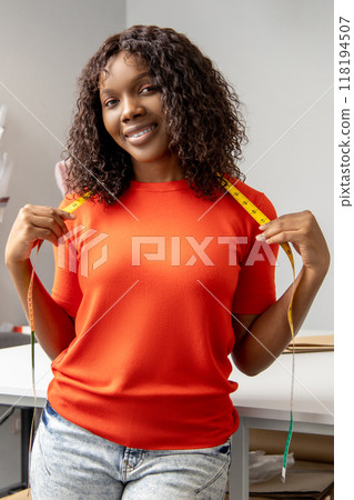 Woman professional tailor standing in designer atelier with measure tape over neck Woman professional tailor standing in designer atelier with measure tape over neck 118194507